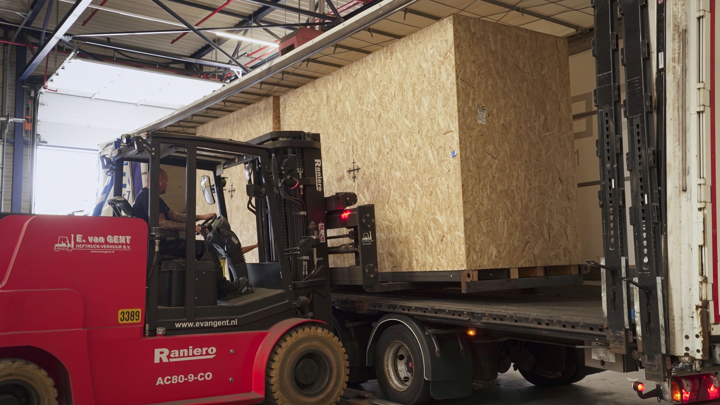Heftruck laadt een grote houten kist in een vrachtwagen aan de laaddock